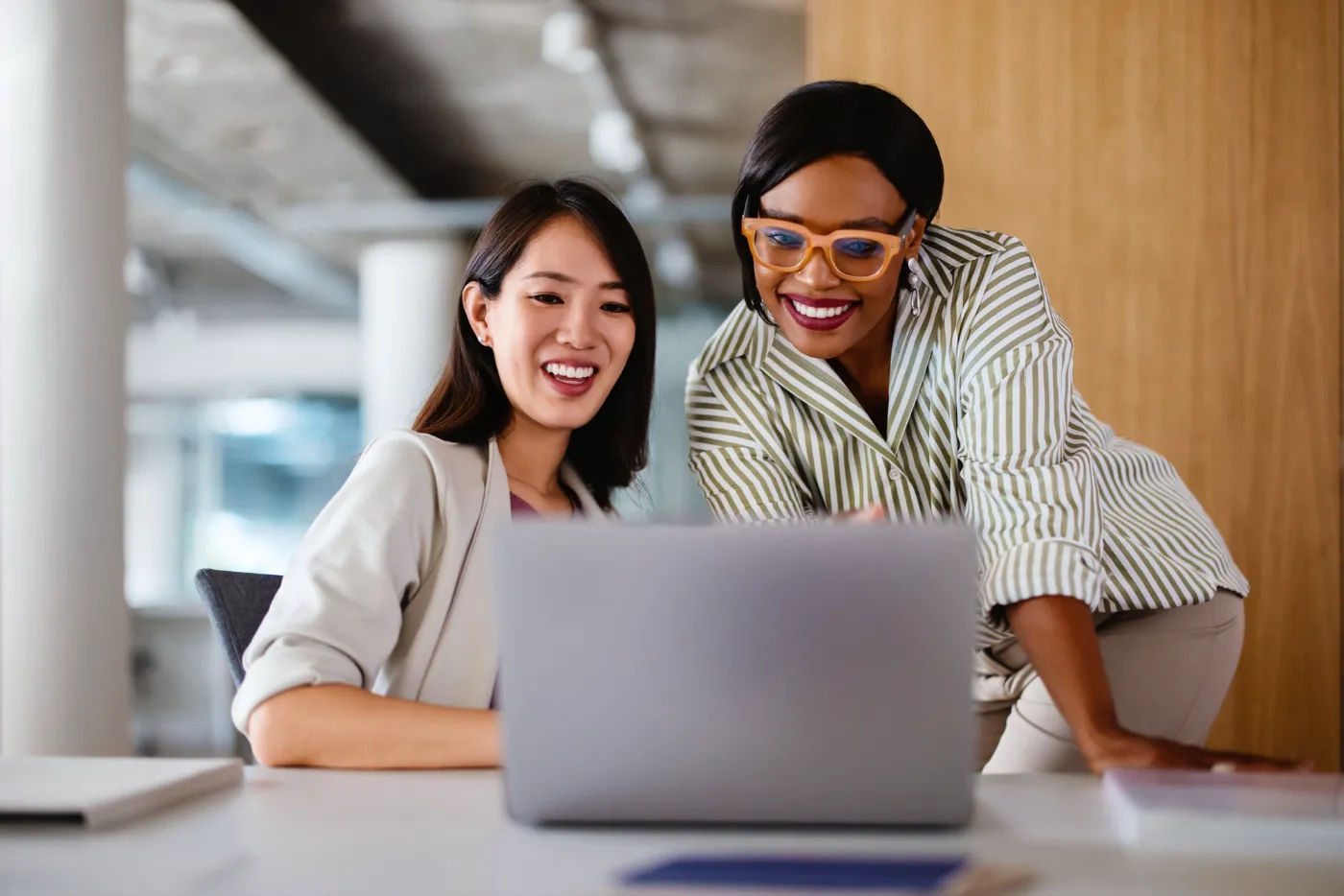 Two colleagues smiling as they look at a laptop together in a bright office