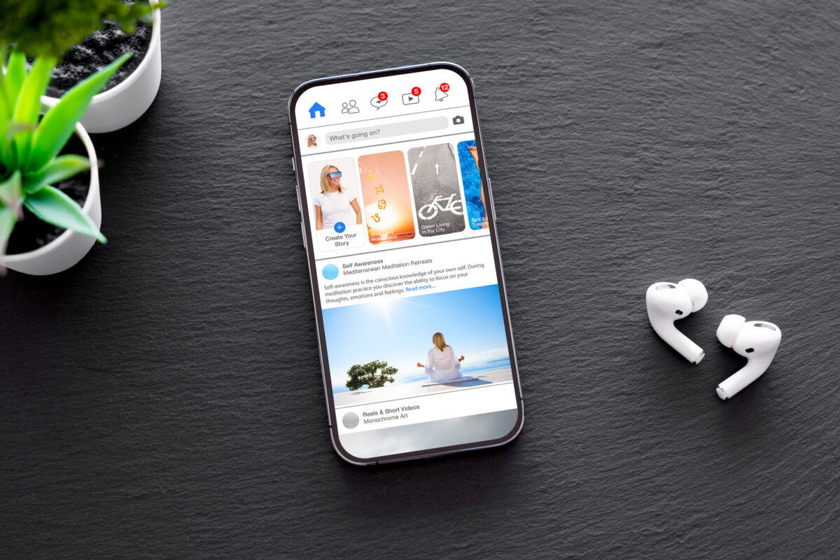 A phone on a desk showing the Facebook main feed.